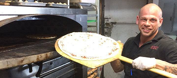 Smiling man placing pizza in oven.